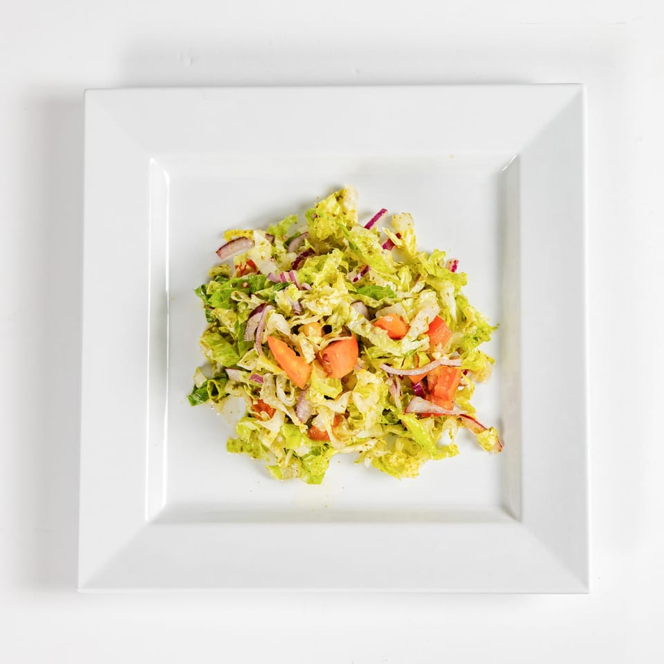 Fresh tossed salad with lettuce, tomatoes, red onions, and dressing on a square white plate.