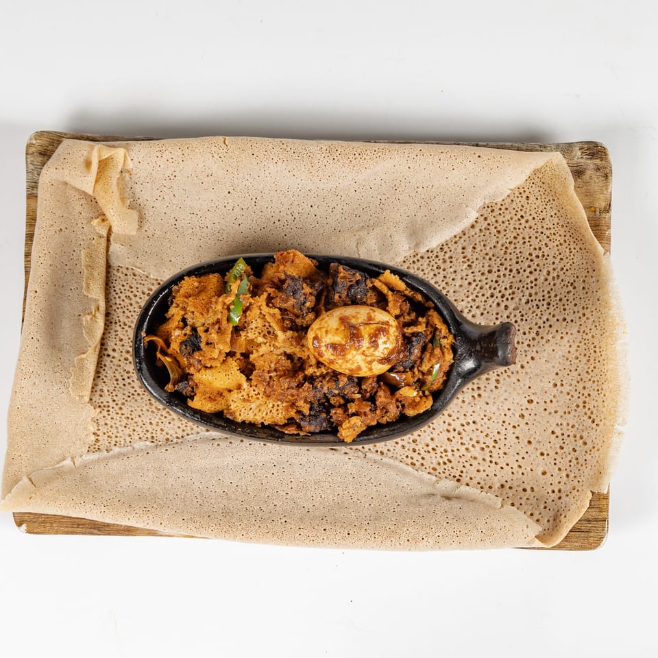 Ethiopian spiced meat and vegetables with a boiled egg served in a black skillet on injera flatbread.