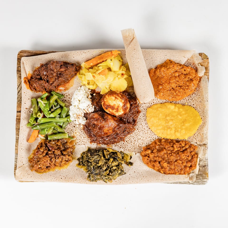 Ethiopian platter served on injera with spiced meats, vegetables, lentils, cheese, and rolled injera.