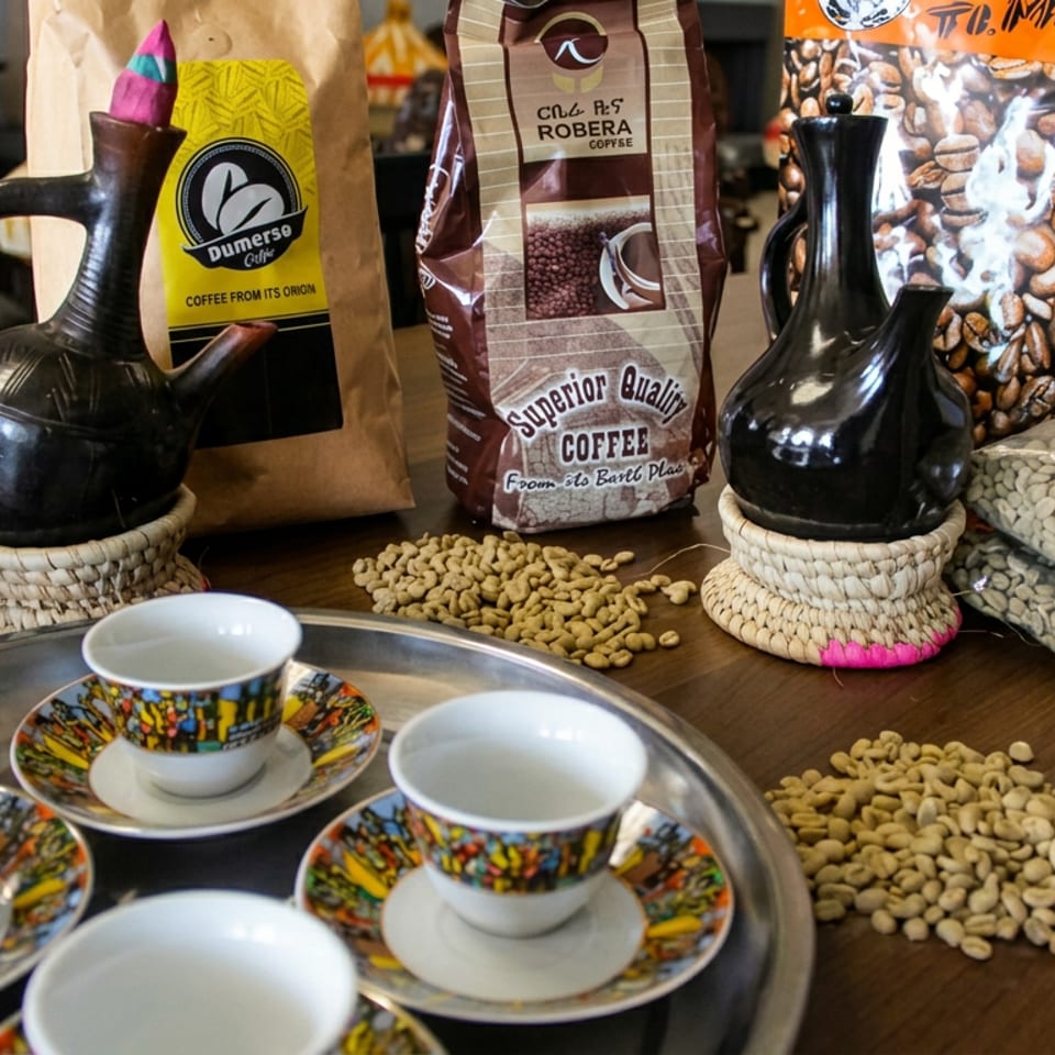 Traditional coffee service with colorful cups, black clay pots, coffee bean bags, and scattered beans on a wooden table.