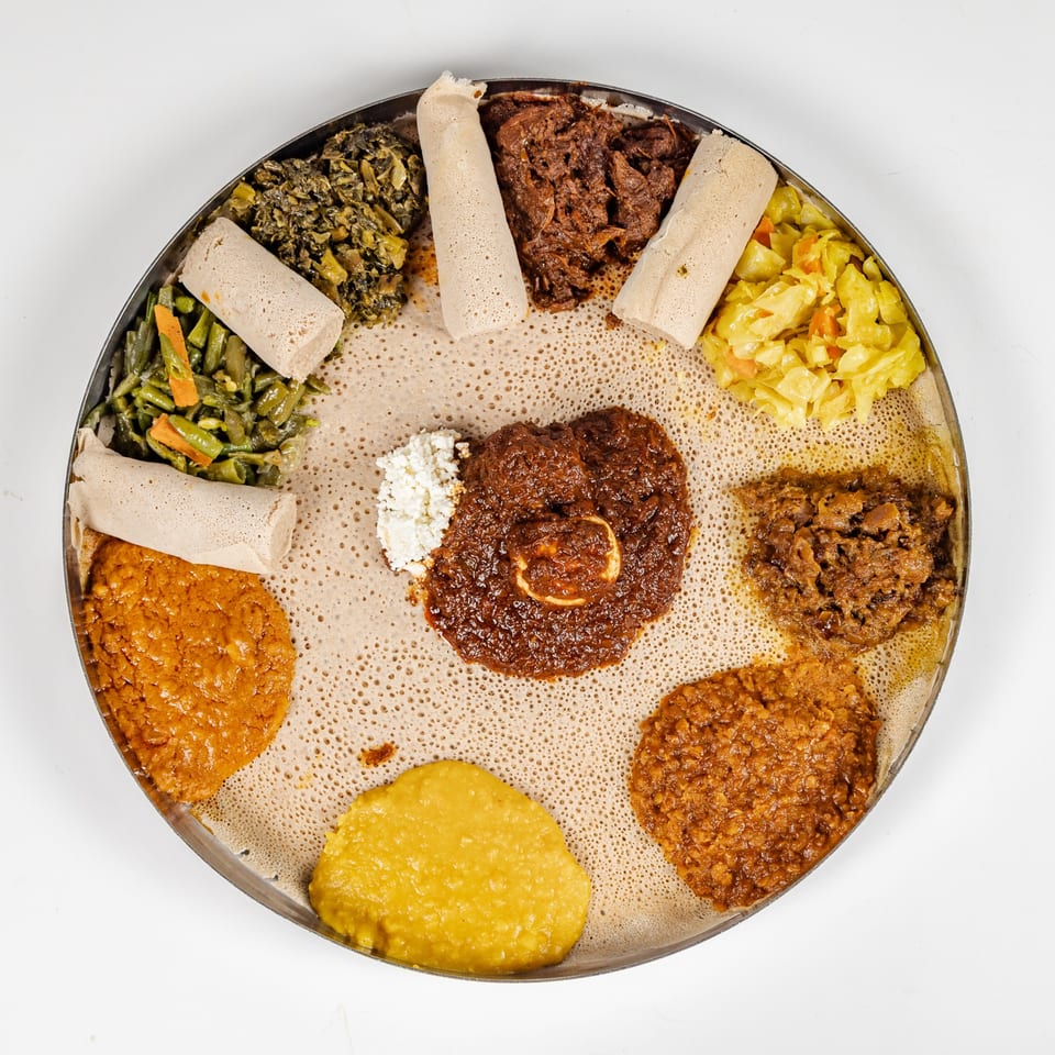 Ethiopian platter of injera topped with assorted stews, vegetables, lentils, greens, and rolled injera pieces.