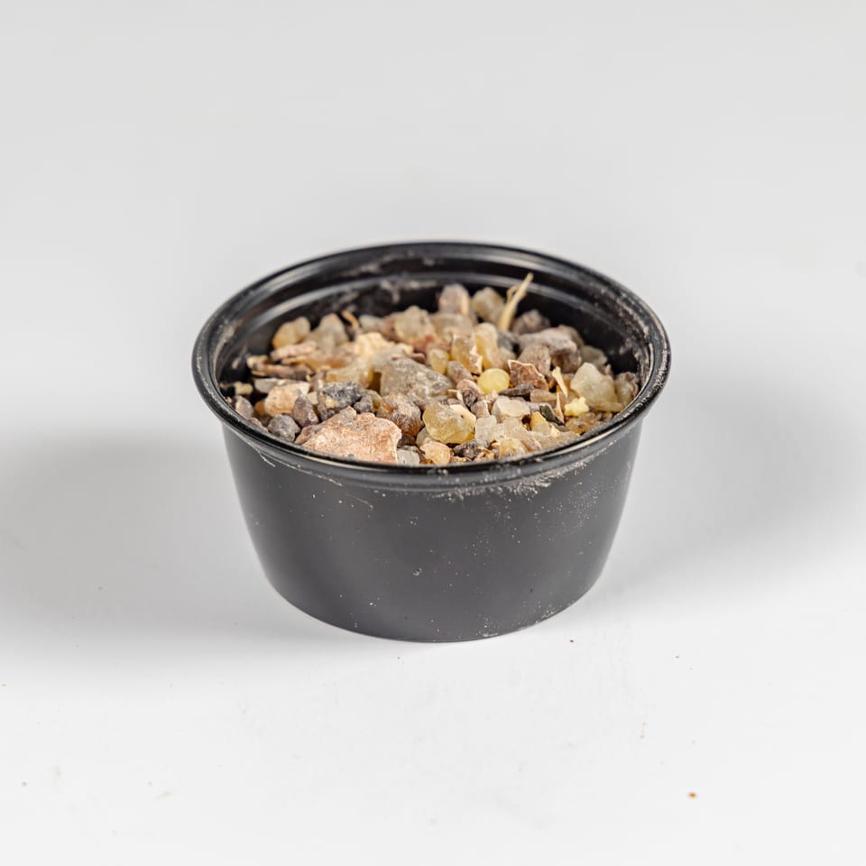 Black bowl filled with assorted dried fruits, nuts, and other snack pieces on a white surface.
