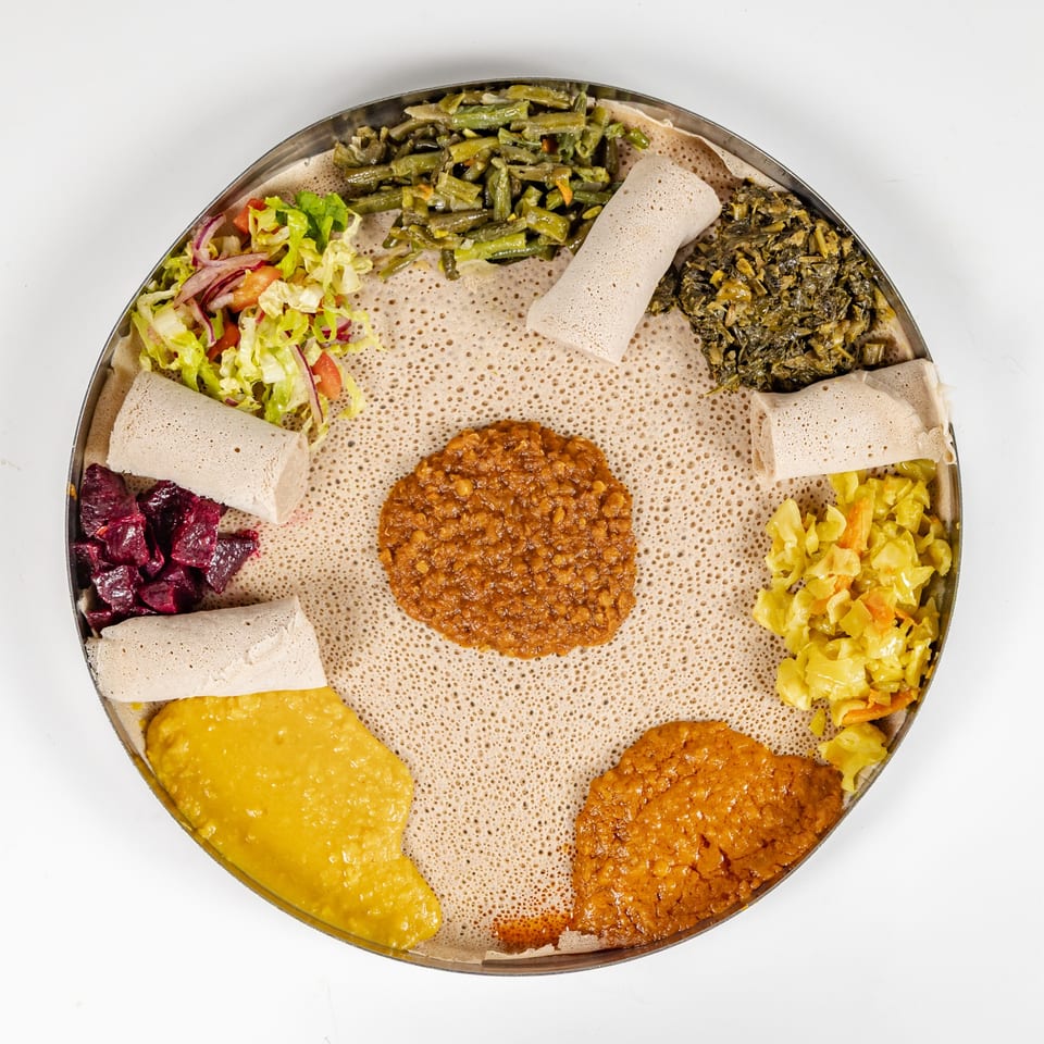 Overhead view of an Ethiopian vegetarian platter with injera, lentils, green beans, cabbage, beets, salad, and stewed greens.