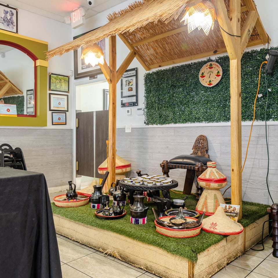 Restaurant interior featuring a thatched-roof seating area, Ethiopian coffee ceremony display, woven baskets, traditional chairs, and greenery-covered walls.