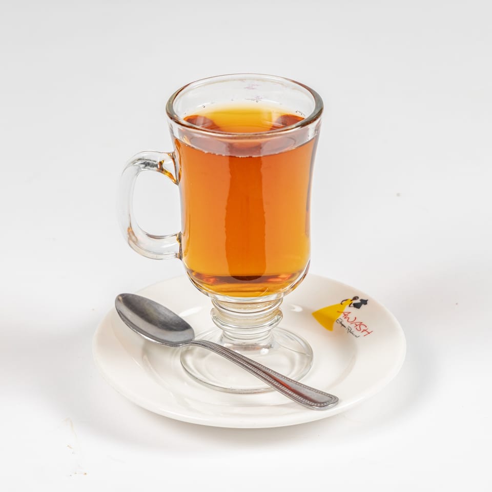 Glass cup of amber tea on a white saucer with a spoon.