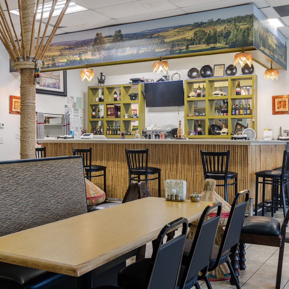 Restaurant dining area with bamboo-accented bar, colorful chairs, hanging lamps, artwork, and countryside mural.
