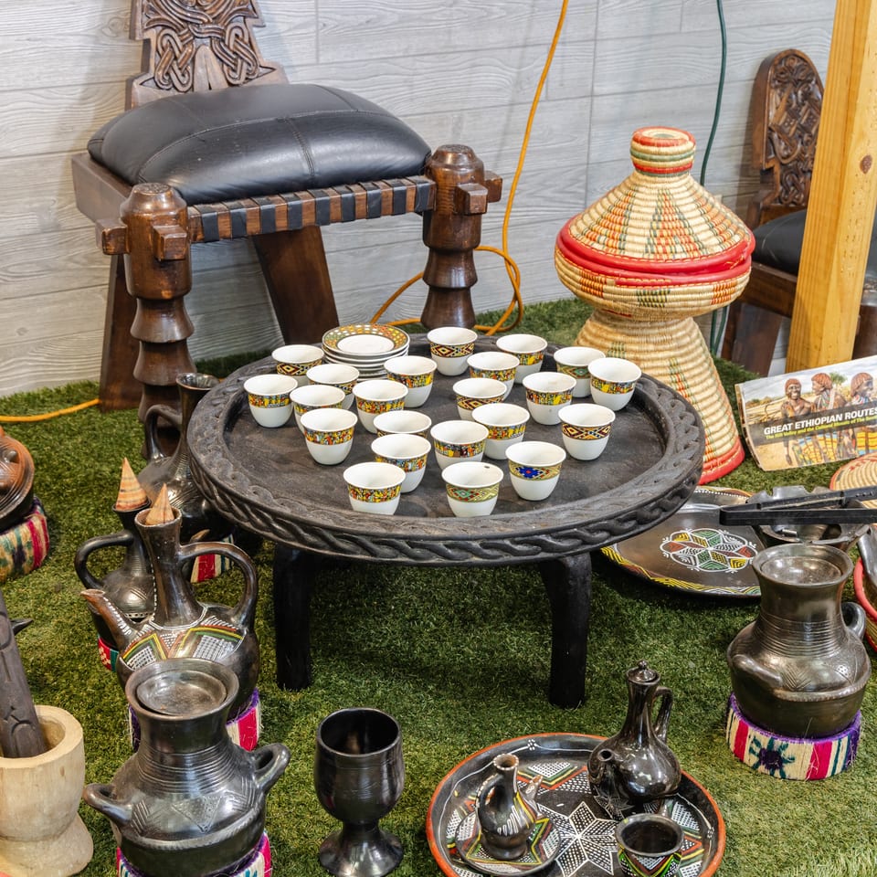 Ethiopian coffee ceremony display with colorful cups, traditional jebena pots, woven baskets, carved chairs, and a central serving table.