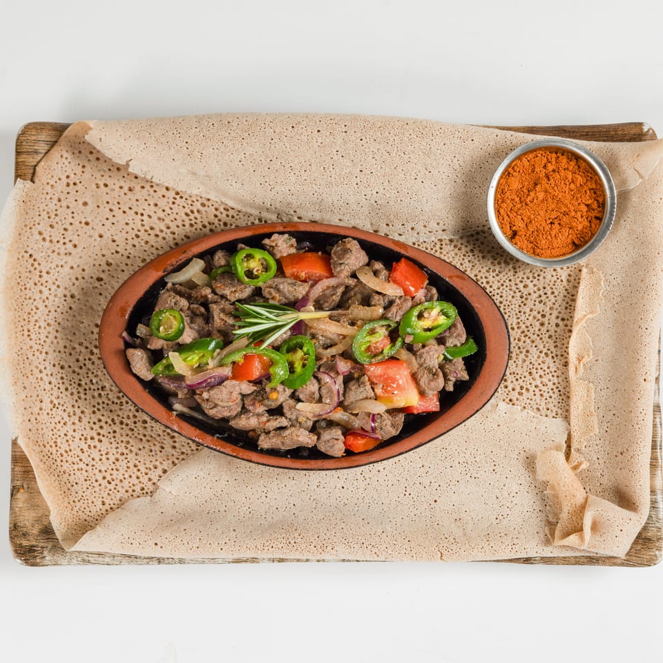 Ethiopian-style beef sauté with peppers, tomatoes, onions, and rosemary served on spongy injera with red spice.