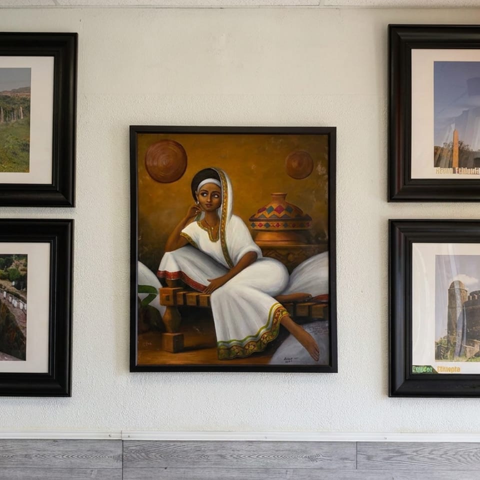 Wall gallery displays framed Ethiopian landscapes, landmarks, and a central painting of a woman in traditional white attire.
