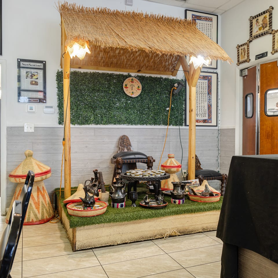 Restaurant interior featuring a thatched-roof display booth, Ethiopian baskets, traditional coffee pots, serving dishes, and cultural artwork.